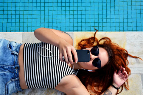 A woman lays by the pool looking at her phone