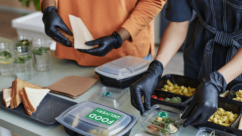 Close up of two young women packing food delivery orders in cafe kitchen, copy space