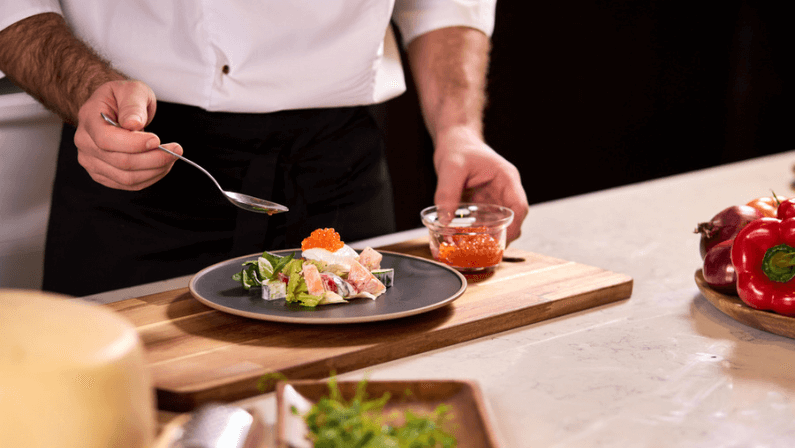 professional cook adds red caviar for salad, making tasty food in restaurant, master class of cooking