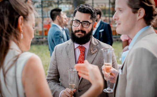 Style Standard founder, James, holding a glass of champagne at an outdoor party looking at a woman speaking
