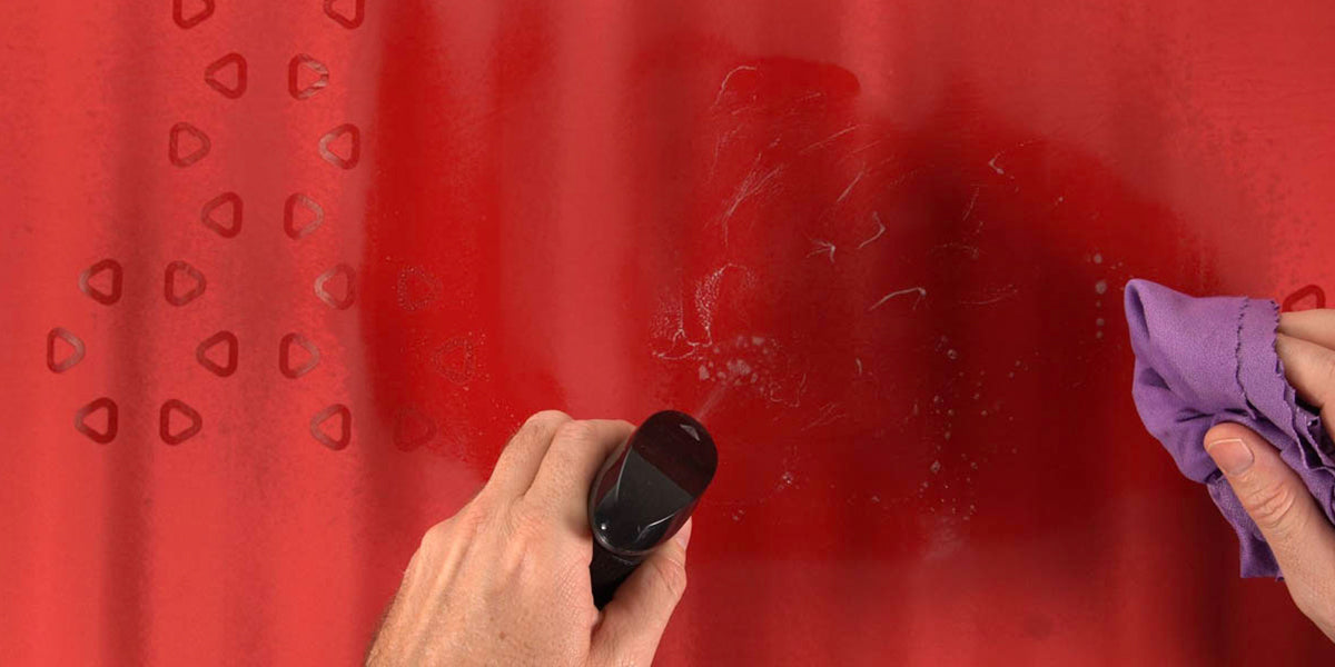 Hands are cleaning a red sleeping pad with a spray bottle and rag