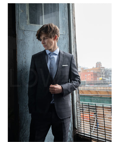 model is wearing spread collar blue shirt with dark navy suit at balcony behind street view