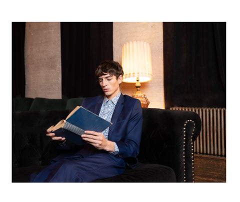 model wearing luxury light blue floral nature color print dress shirt with navy suit while reading books at comfy couch
