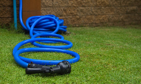 Blue hose with a hose attachment laying on a green lawn