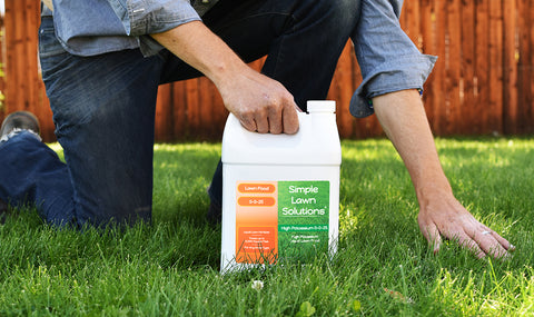 Man kneeling on a green lawn holding Simple Lawn Solutions fertilizer