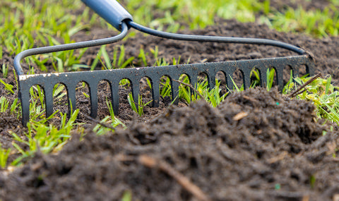 Close-up of a metal rake spreading soil across a lawn 