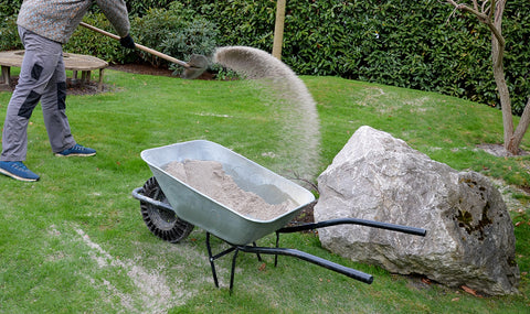 Man using soil and a wheelbarrow to topdress lawn