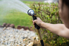 person watering lawn with hose holding it over grass and rock area