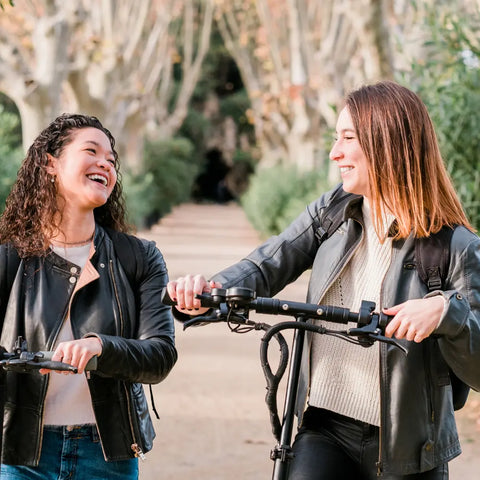 Mujeres universitarias en scooters charlando, imagen de archivo Crédito: Canva