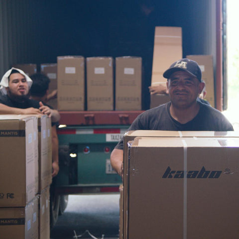 Men unloading scooter boxes from a truck, smiling to camera