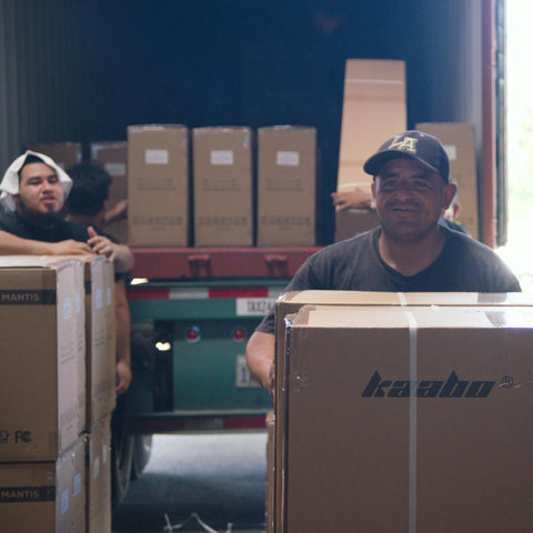 Hombres descargando cajas de scooters de un camión, sonriendo a la cámara