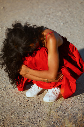 A woman in a red dress curled up in the fetal position, as if experiencing cramps