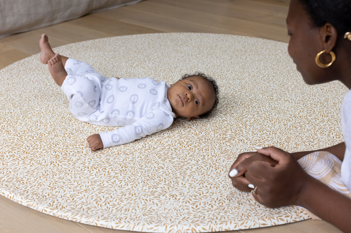 baby laying on back on comfortable foam play mat by Totter + Tumble iconic Standen motif