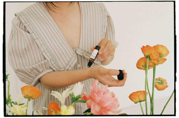 mujer rodeada de flores aplicándose un rollon de aromaterapia