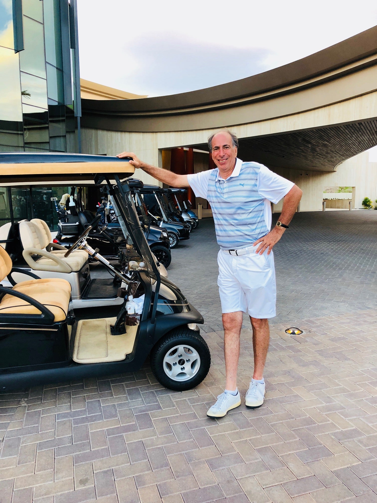 An older guy standing next to a golf cart wearing a polo and white shorts after hiring a stylist