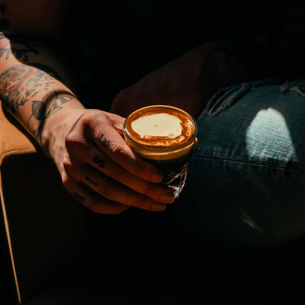 tattooed person holding a vietnamese coffee with rum in their hand