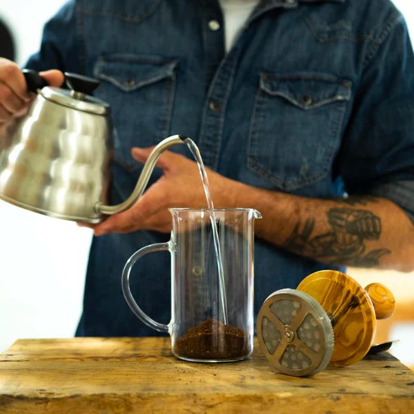 person pouring water over ground coffee in french press