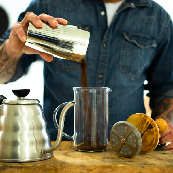 person dropping ground coffee in french press