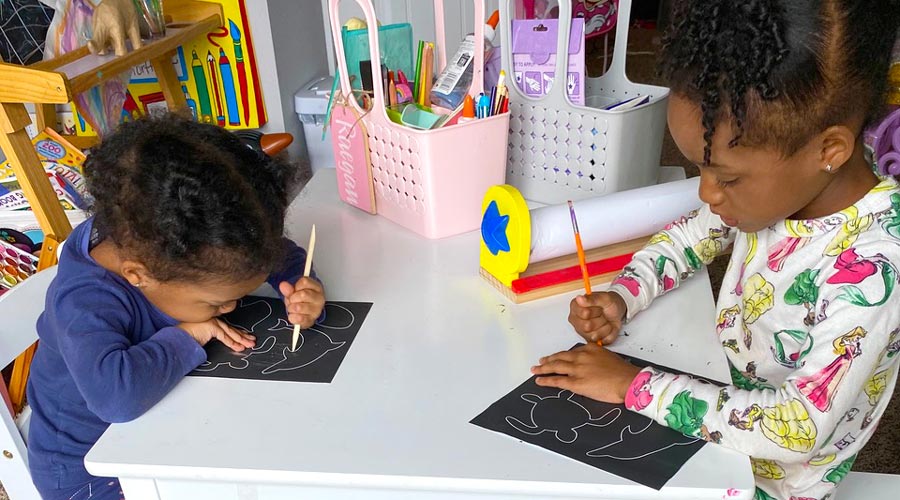 two girls sitting at white table using scratch and scribble art kits