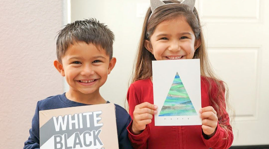 two smiling kids holding craft paper and holiday card in front of white background