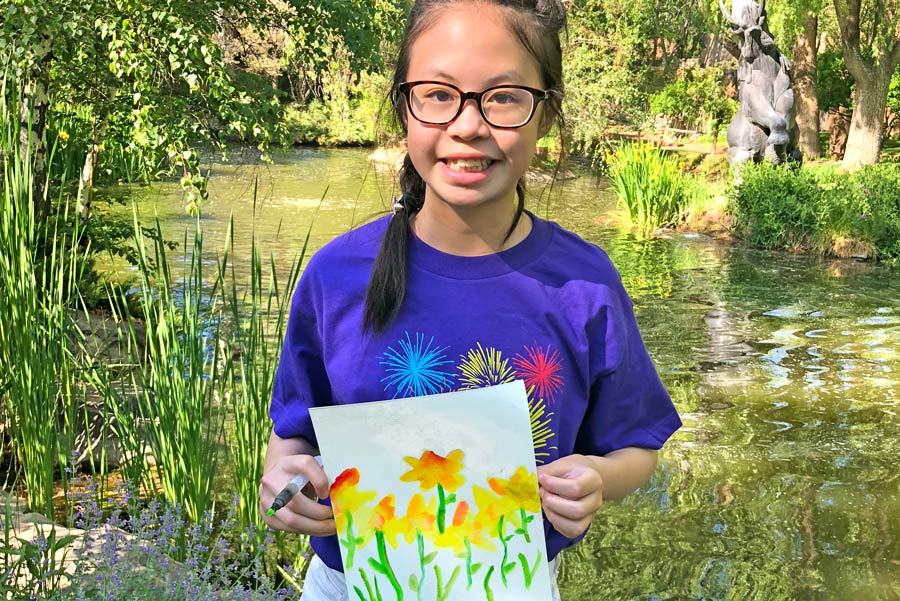 Girl holding up her watercolor painting of yellow flowers