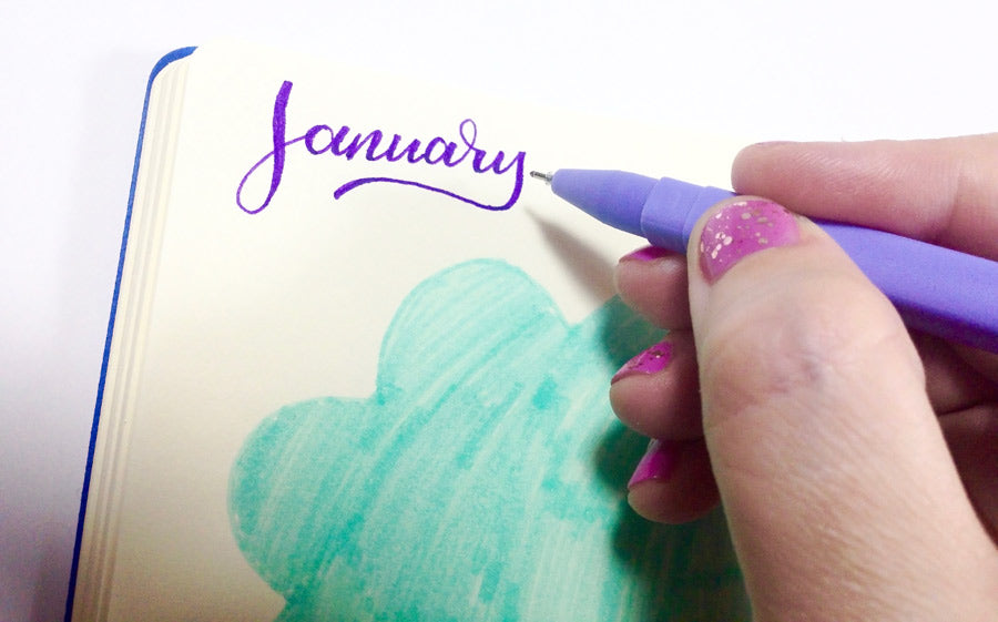 Brush lettering "January" in a DIY journal with a colored gel pen