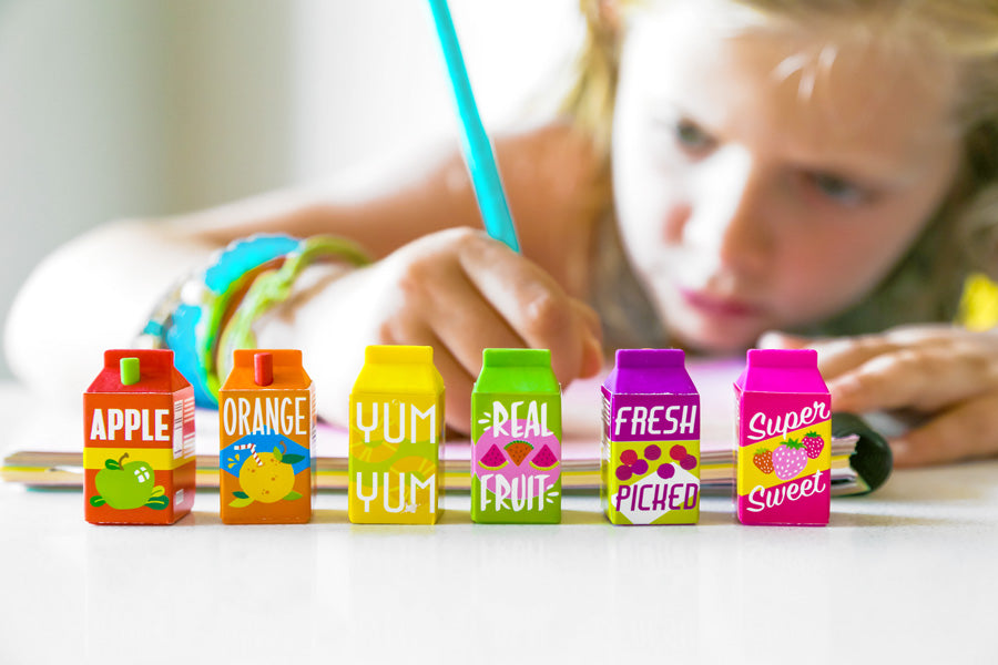 Girl writing in workbook with lil' Juicies scented erasers in front