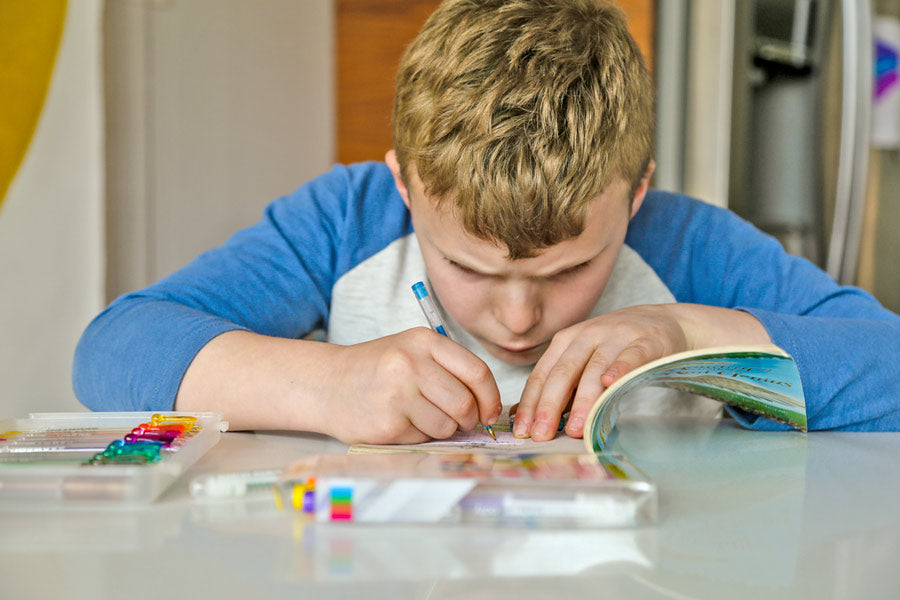 Boy writing with gel pens on a sticky note in a book