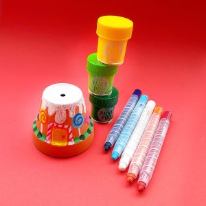 Twisty oil pastel stix and lil poster paint pods next to a colorful pot on a red background