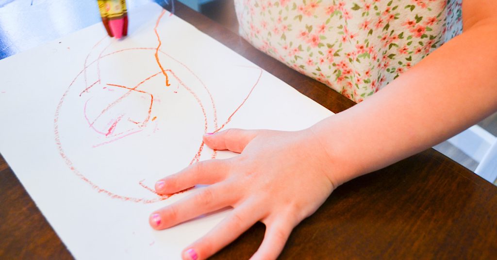 child hands using crayons to color on white paper