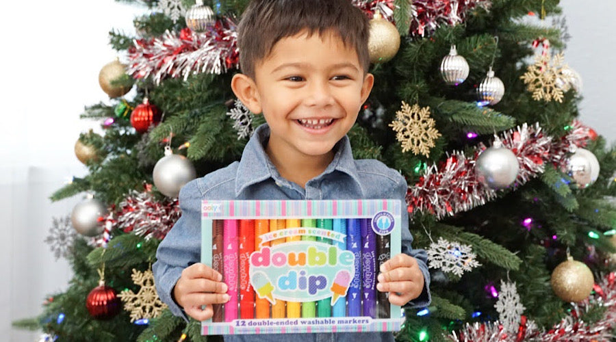 smiling boy holding markers in front of christmas tree
