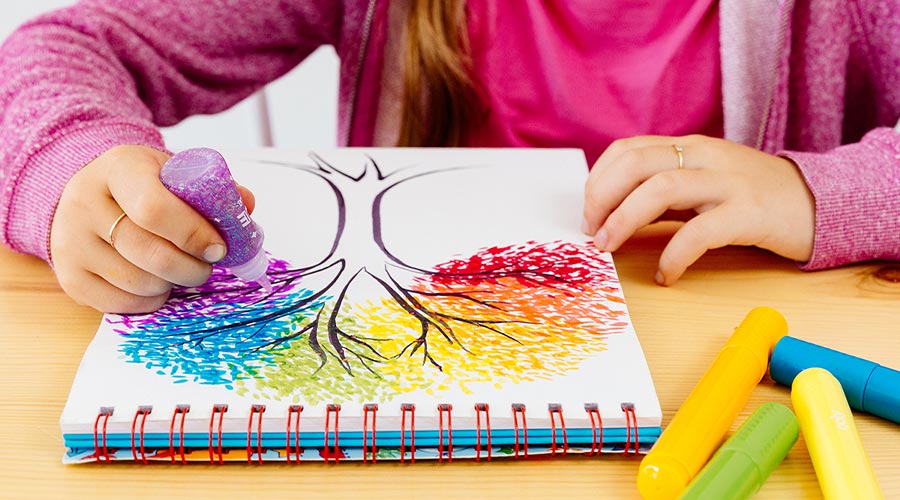 child sitting at table creating rainbow tree with purple glitter glue