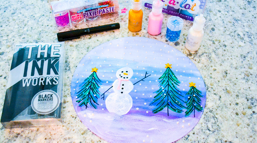 snowman and trees on blue and purple background surrounded by craft paint and black markers