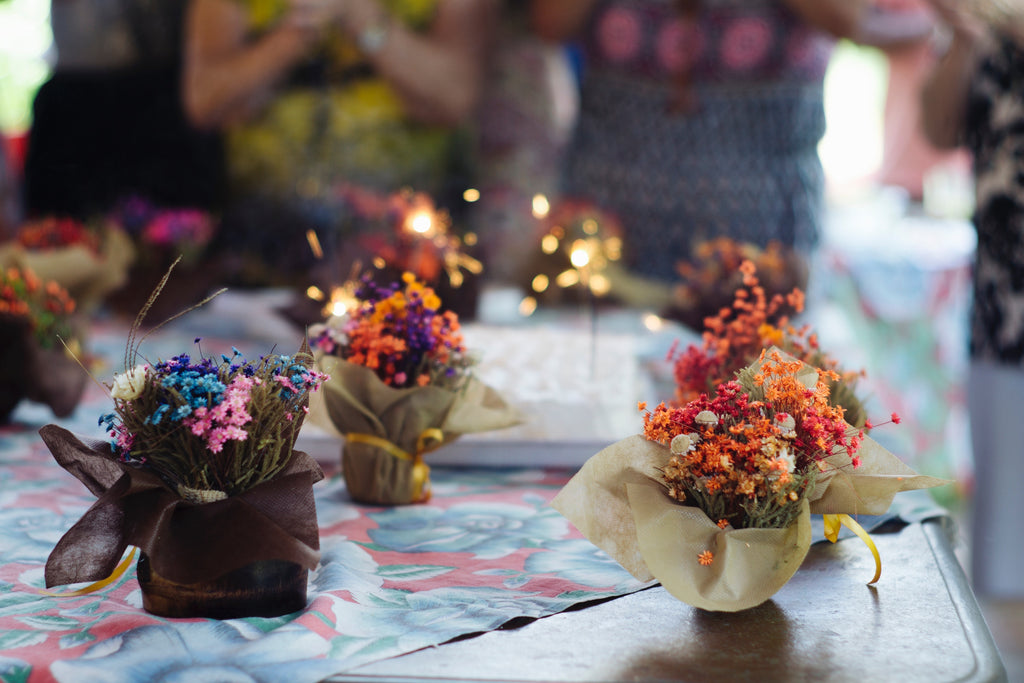 Dried flower arrangements on a table with soft - focus people and sparklers in the background