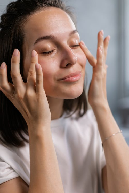 A woman massaging Allurials' organic carrot seed oil under the eyes