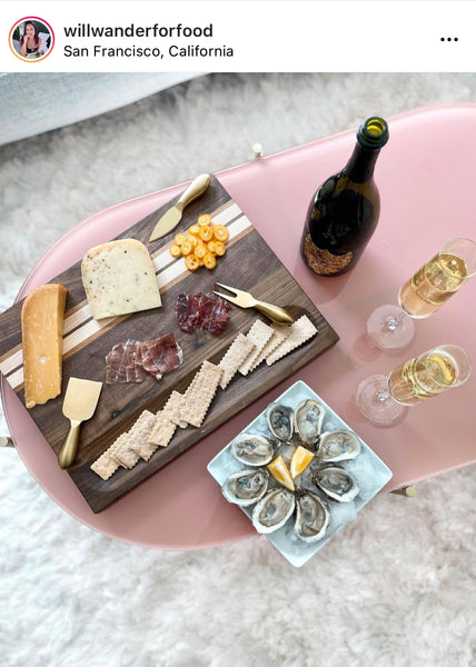 Crackers and cheese spread on a walnut wood cutting board with champagne and oysters