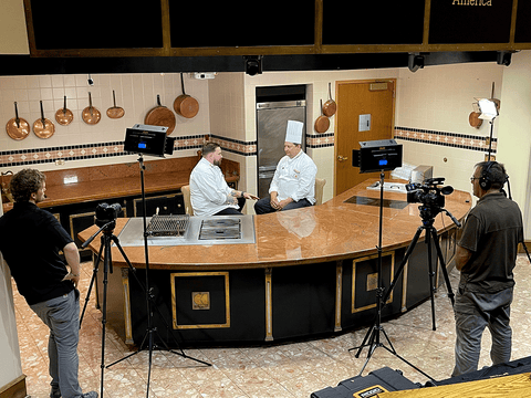 film crew and commercial kitchen with two chefs seated and talking