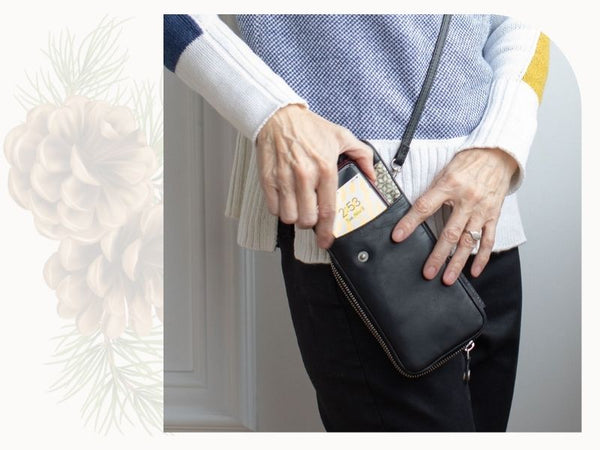 A woman puts a phone in a black leather phone pouch.