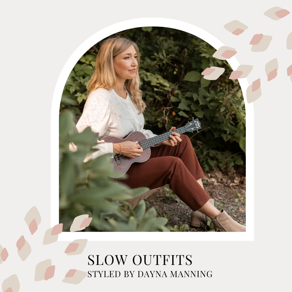 Slow outfits, styled by Dayna Manning. Dayna is shown sitting on a riverbank holding a guitar, wearing rust coloured pants and an ecru long sleeved blouse.