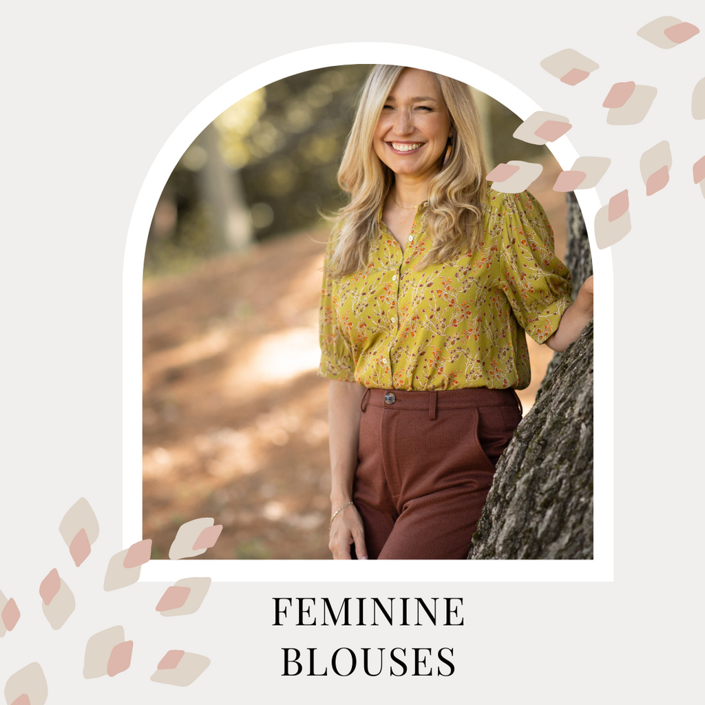 Feminine Blouses. Dayna wears a mustard coloured blouse with a small floral print. She has one hand on a tree trunk and smiles wide.