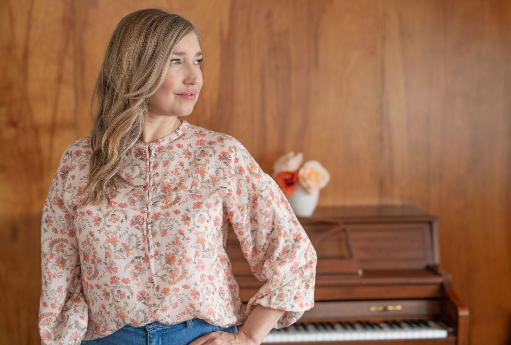 Dayna Manning wears a peach coloured blouse with a small floral print. A piano is shown in the background.