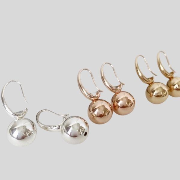 Three pairs of earrings are shown. They are small metallic balls. One pair is silver, one pair is rose gold, and one pair is gold.