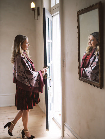 Dayna opens the door to a guest wearing a silk scarf around her shoulders.