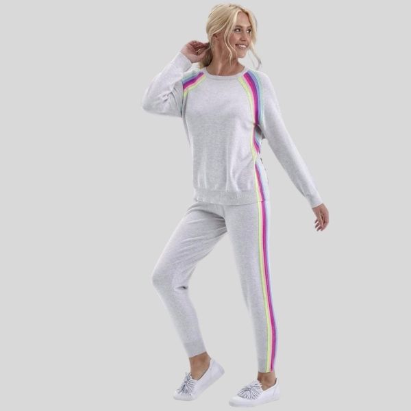 A woman wears a white jogging suit with rainbow stripes on the shoulders and down the legs.