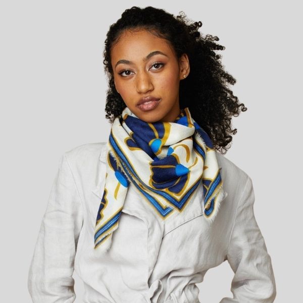 A woman wears a scarf with a blue and gold pattern around her neck..