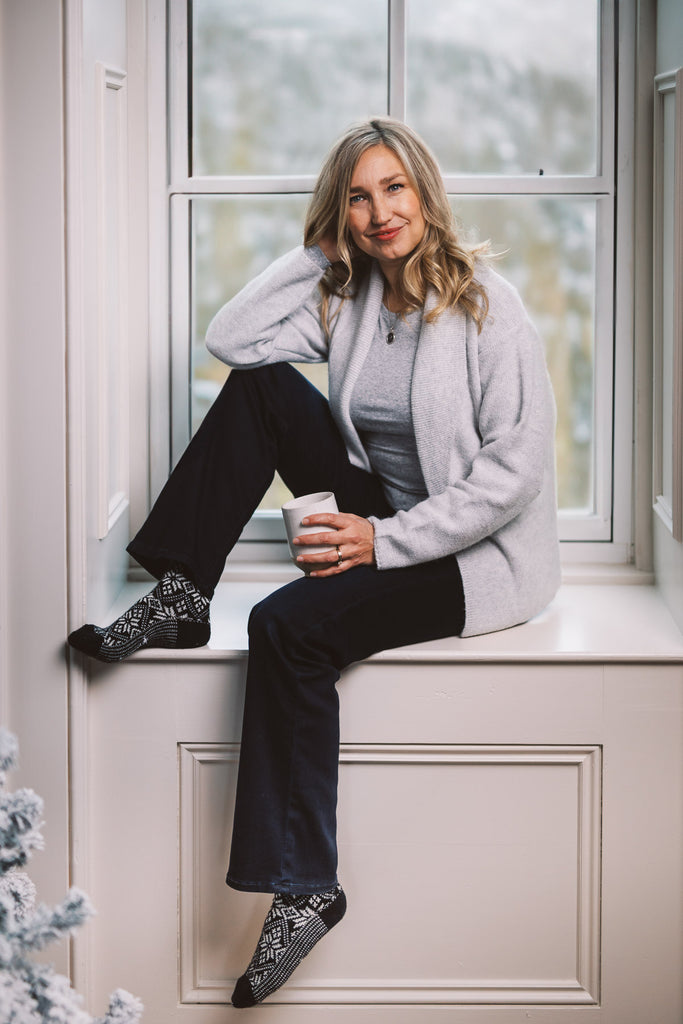 Dayna Manning sits in a window sill holding a cup of tea. She's wearing Smartwool socks with a snowflake pattern.