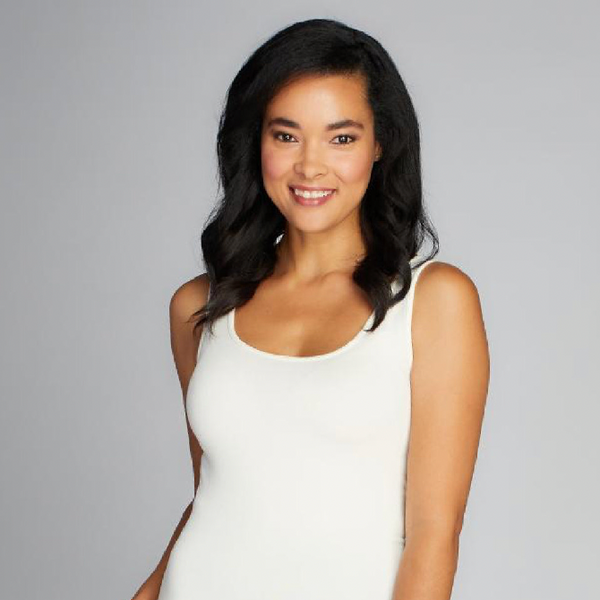 A woman wears an ivory coloured tank top. it has a long body and thick shoulder straps. It's very fitted.