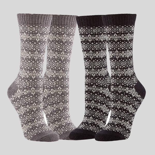Two pairs of socks are shown. They have a snowflake design. The pair on the left is grey with white snowflakes, and the pair on the right is black with white snowflakes..