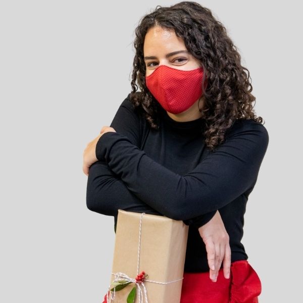 A woman wears a red mask. She holds a wrapped Christmas gift.
