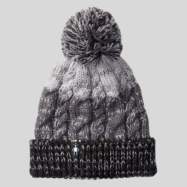 A pompom toque is shown. It has three stripes. The top is light grey, the middle is dark grey, and the band of the hat is heathered black. It has a pompom.